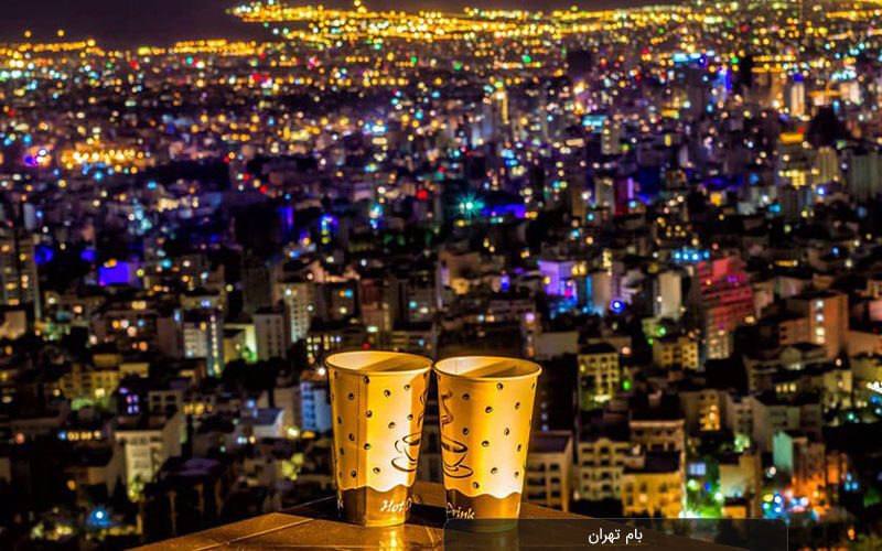 تصویری از منظره ای تهران عدد لیوان نوشیدنی گرم قرار دارد که نشان دهنده دختر و پسر عاشقی هست که کنار هم نشسته اند و در یکی از زیباترین جاهای دیدنی تهران نشسته اند.